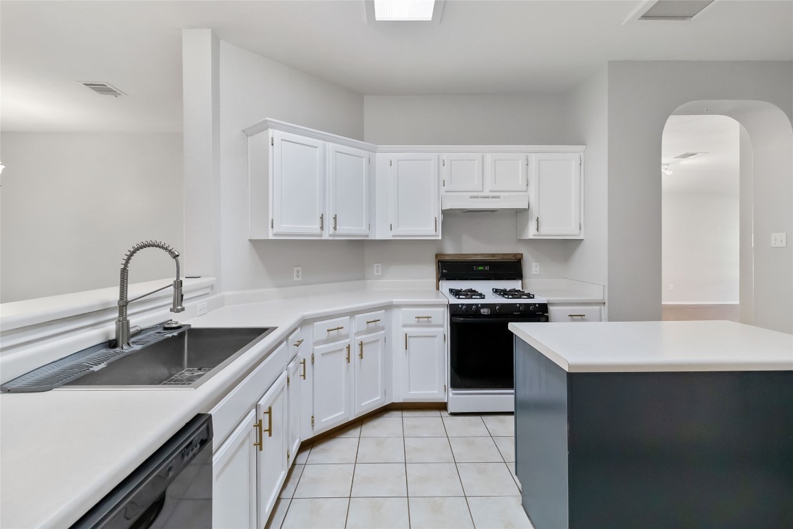 1320 Lochaline Loop Pflugerville, TX 78660 - Photo 10 of 35 Kitchen with white cabinets, gas range oven, light countertops, arched walkways, and light tile patterned floors