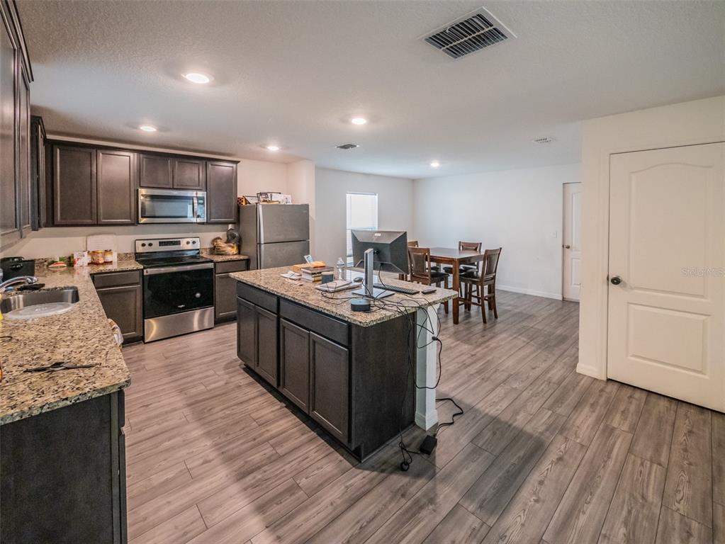 938 Mansfield Road Tavares, FL 32778 - Photo 7 of 25 a large kitchen with stainless steel appliances kitchen island granite countertop a stove a refrigerator a sink a dining table and chairs with wooden floor