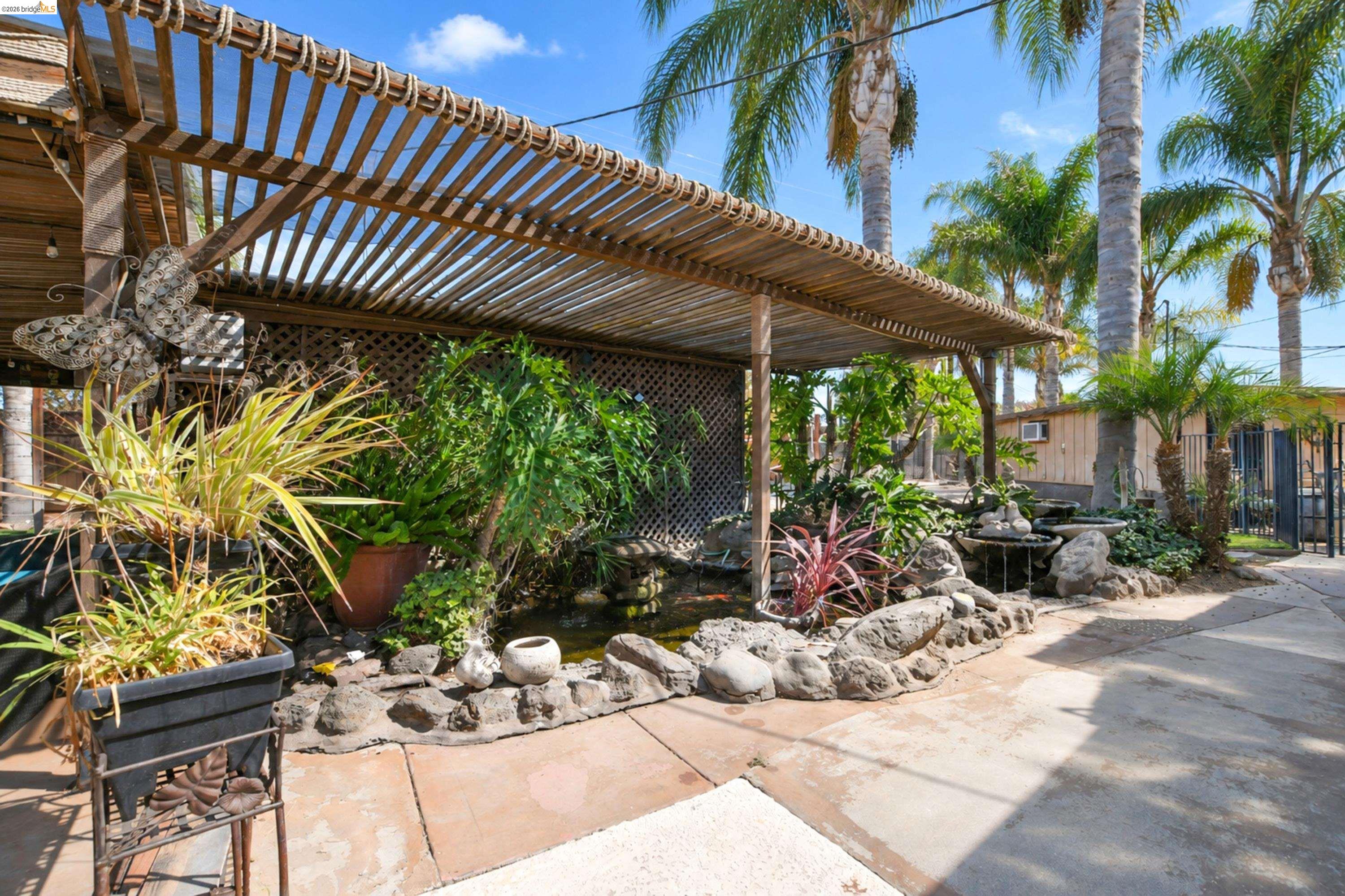 340 West Bolton Road Oakley, CA 94561 - Photo 57 of 87 Wood pergola structure with slatted roof, rock-lined water feature, lush landscaping, and mature palm trees