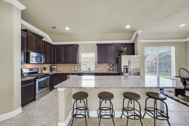 a kitchen with stainless steel appliances granite countertop a stove top oven a sink dishwasher and chairs with wooden cabinets