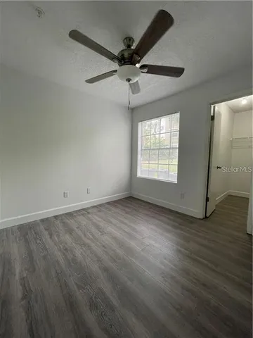 an empty room with wooden floor fan and windows