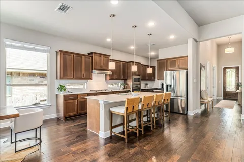 a kitchen with stainless steel appliances granite countertop a refrigerator a stove top oven and a dining table with wooden floor
