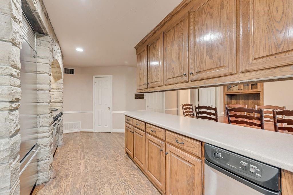 2 Eastshore Road Heath, TX 75032 - Photo 17 of 40 Wood-finish flooring, stone-clad archway, oak cabinetry, light-toned countertops, and a built-in stainless steel dishwasher