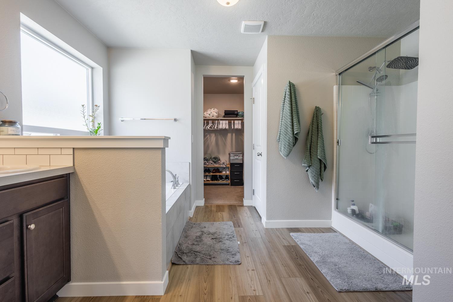 12623 Shadow Peak Street Caldwell, ID 83607 - Photo 31 of 50 Bathroom featuring a built-in soaking tub, glass-enclosed shower, dark wood-finish vanity with a white countertop and subway tile backsplash, a large horizontal window, and wood-finish flooring