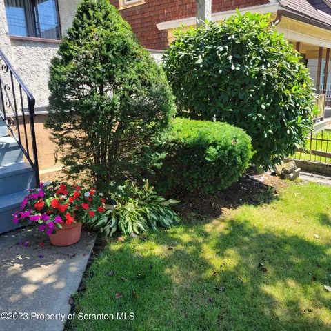a bunch of flowers and trees in front of yellow house
