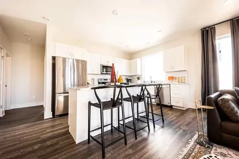 a open kitchen with stainless steel appliances granite countertop a refrigerator a stove a dining table and chairs with wooden floor