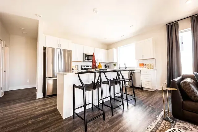 a open kitchen with stainless steel appliances granite countertop a refrigerator a stove a dining table and chairs with wooden floor