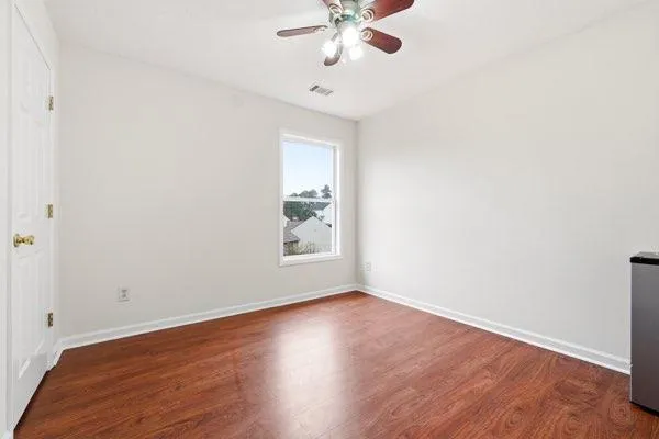an empty room with wooden floor fan and windows