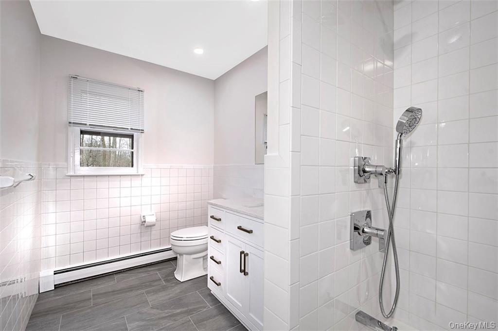 74 Edgewood Road Ossining, NY 10562 - Photo 16 of 29 Full bathroom featuring white subway tile, a white vanity with dark hardware, a walk-in shower with a handheld showerhead, and wood-finish tile flooring