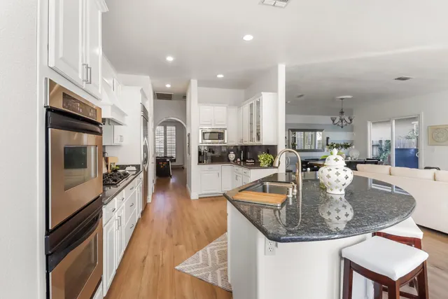 a large kitchen with stainless steel appliances granite countertop a sink dishwasher a refrigerator and a dining table with wooden floor