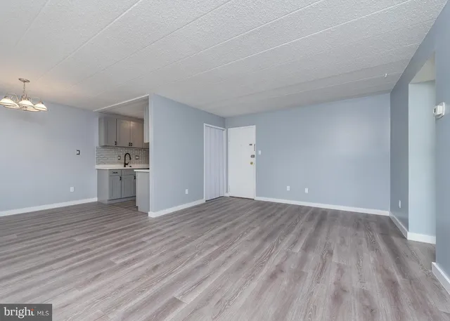 a view of empty room with wooden floor and kitchen