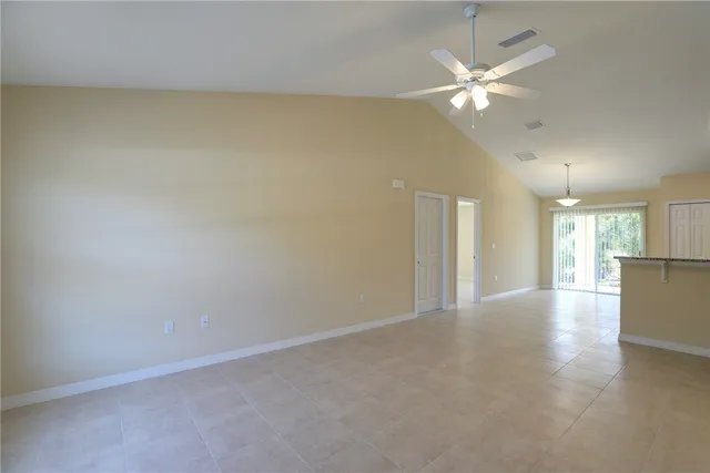 an empty room with chandelier fan and windows