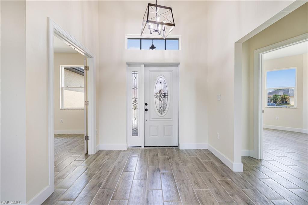 4909 Berryman Street Lehigh Acres, FL 33971 - Photo 3 of 30 Foyer entrance featuring wood tiled floors, a chandelier, and a towering ceiling