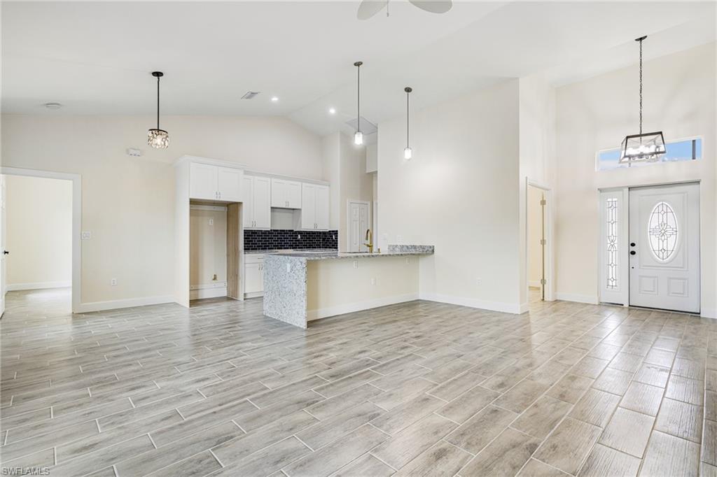 4909 Berryman Street Lehigh Acres, FL 33971 - Photo 30 of 30 Kitchen with a peninsula, high vaulted ceiling, decorative light fixtures, white cabinets, and open floor plan