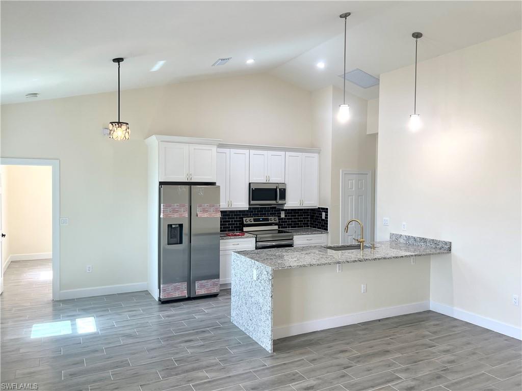 4909 Berryman Street Lehigh Acres, FL 33971 - Photo 4 of 30 Kitchen featuring stainless steel appliances, light stone counters, high vaulted ceiling, a peninsula, and white cabinets