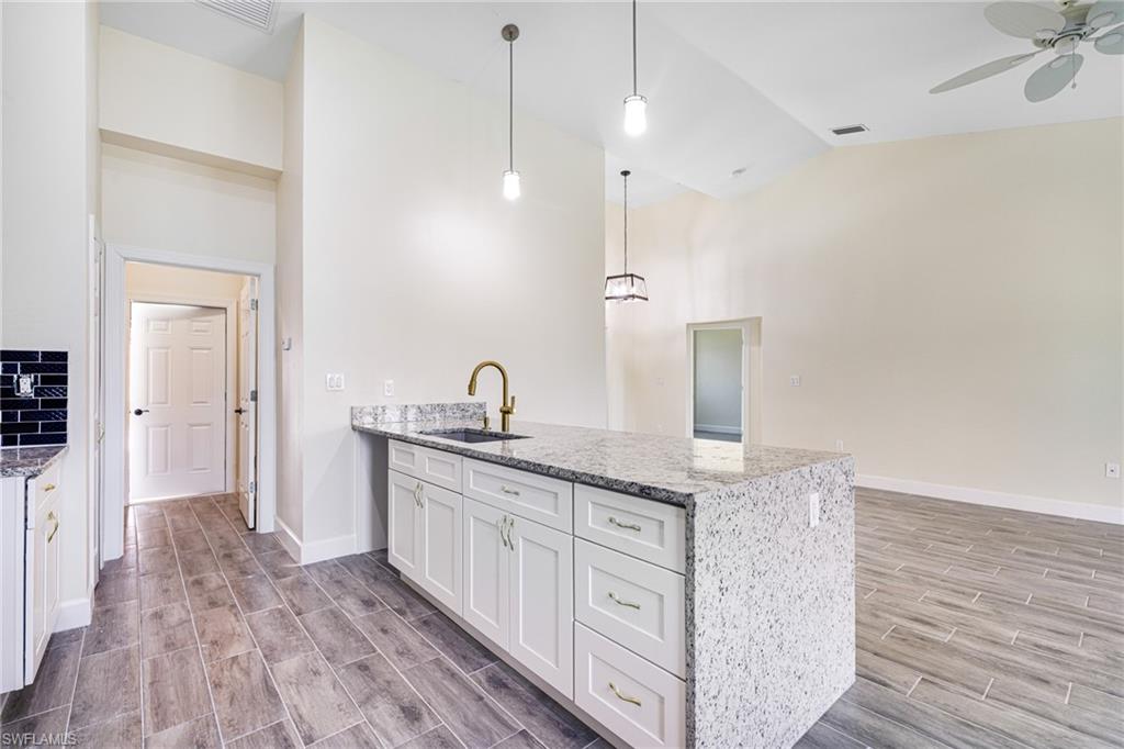 4909 Berryman Street Lehigh Acres, FL 33971 - Photo 5 of 30 Kitchen featuring a peninsula, wood finish floors, light stone counters, decorative light fixtures, and white cabinetry