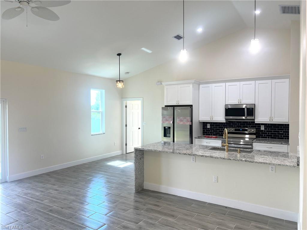 4909 Berryman Street Lehigh Acres, FL 33971 - Photo 6 of 30 Kitchen with light stone countertops, pendant lighting, white cabinets, wood tiled floors, and high vaulted ceiling