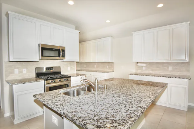 a kitchen with granite countertop a stove top oven a sink a counter space and cabinets