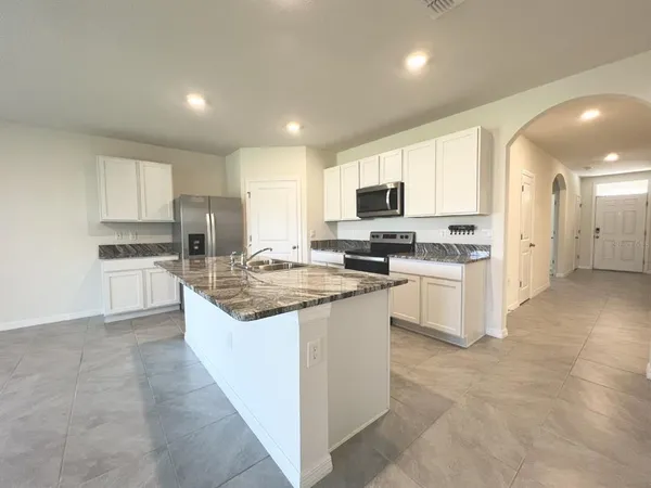 a kitchen with stainless steel appliances granite countertop a stove top oven a sink a refrigerator and white cabinets