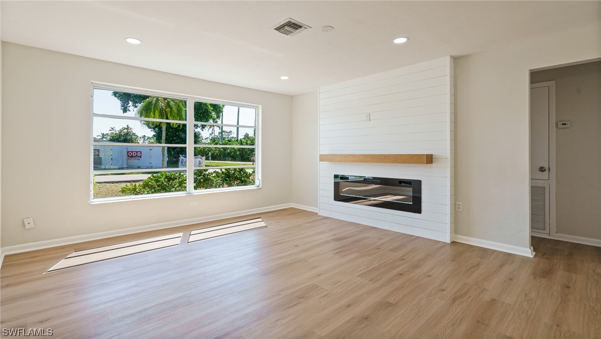 8631 Exeter Street Fort Myers, FL 33907 - Photo 4 of 23 an empty room with wooden floor a fireplace and windows