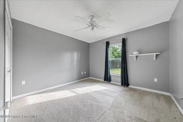 a view of an empty room with window and chandelier fan