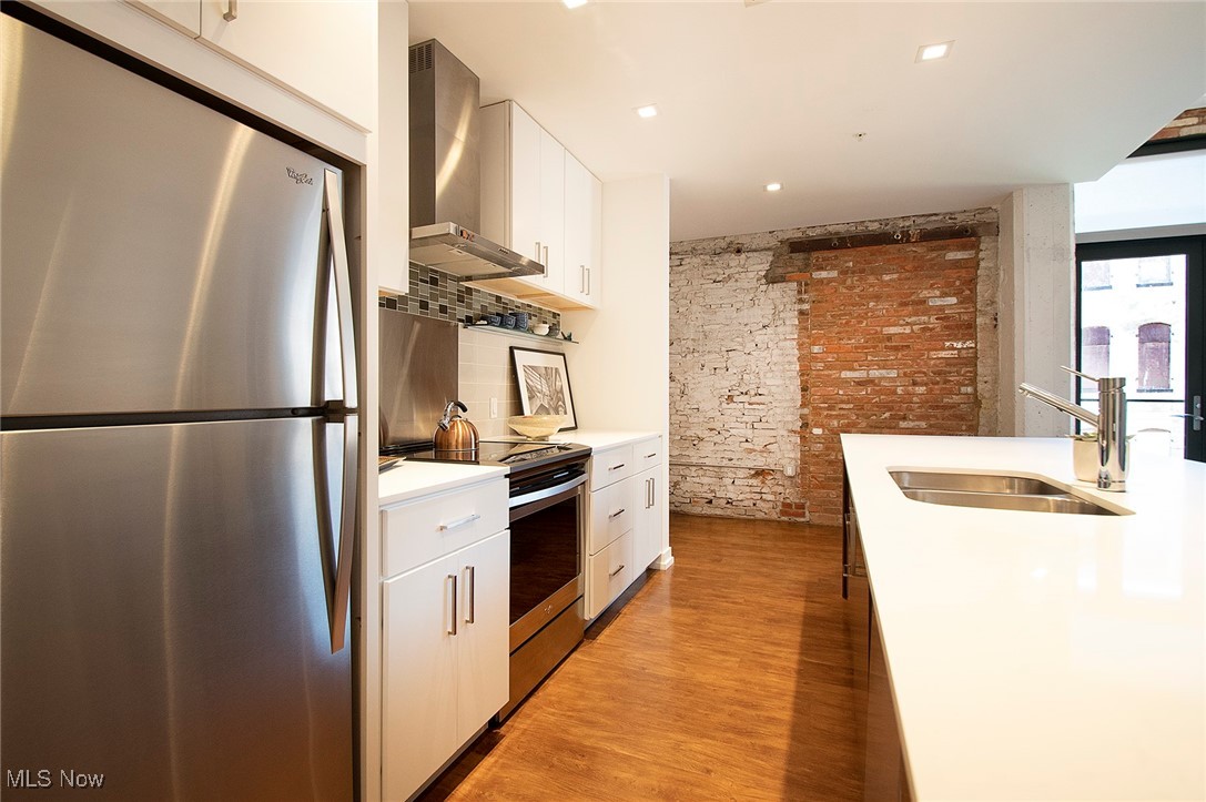 725 Johnson Court, Unit 220 Cleveland, OH 44113 - Photo 7 of 25 Kitchen featuring appliances with stainless steel finishes, wall chimney exhaust hood, light countertops, light wood-style floors, and white cabinetry
