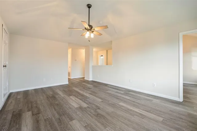 a view of an empty room with chandelier fan and wooden floor
