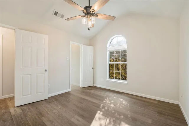 an empty room with wooden floor chandelier fan and windows
