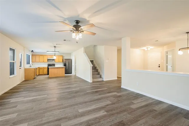 a view of an empty room with wooden floor and a kitchen