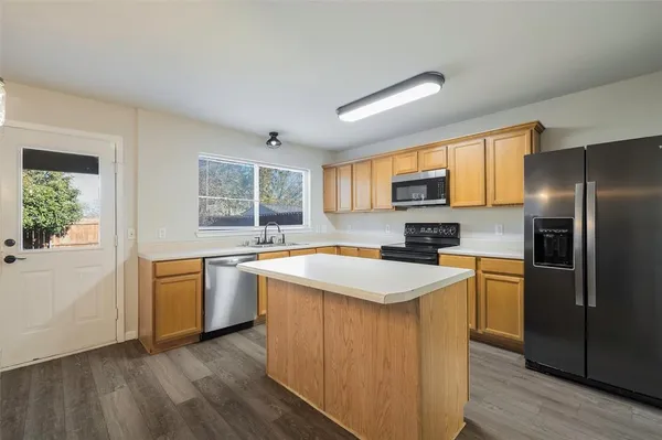 a kitchen with stainless steel appliances granite countertop a refrigerator a stove top oven a sink dishwasher and wooden cabinets with wooden floor