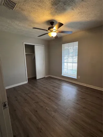 an empty room with wooden floor chandelier fan and windows