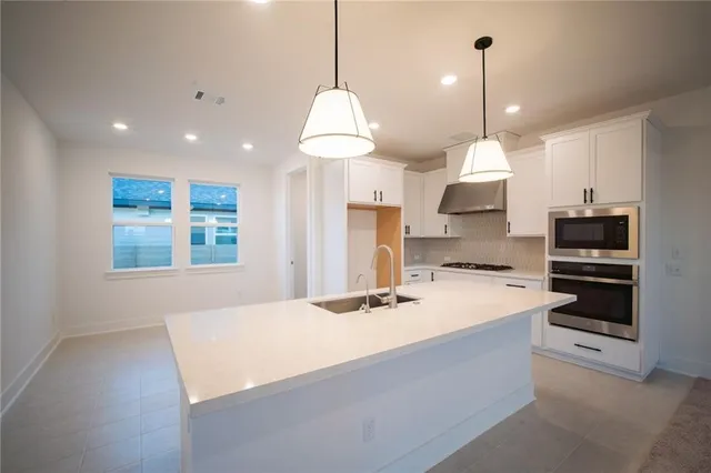a kitchen with stainless steel appliances a stove a sink a microwave a refrigerator and white cabinets