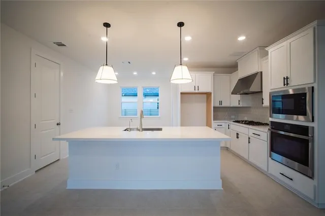 a view of an empty room with kitchen view and a ceiling fan