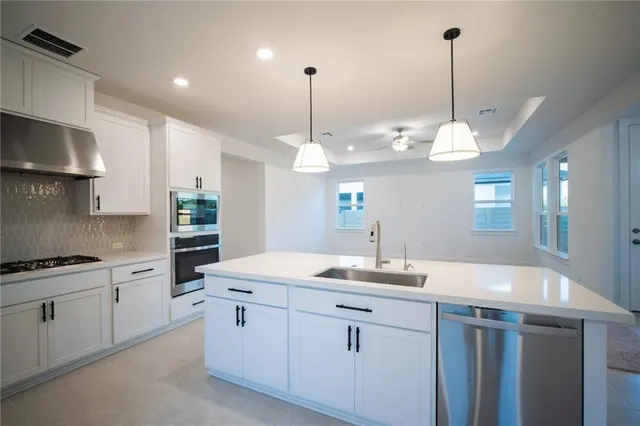 a kitchen with stainless steel appliances kitchen island granite countertop a stove a sink a refrigerator and white cabinets with wooden floor