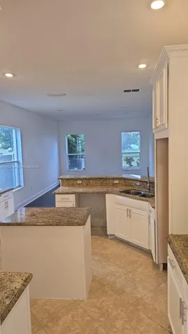 a kitchen with kitchen island granite countertop a sink and white cabinets