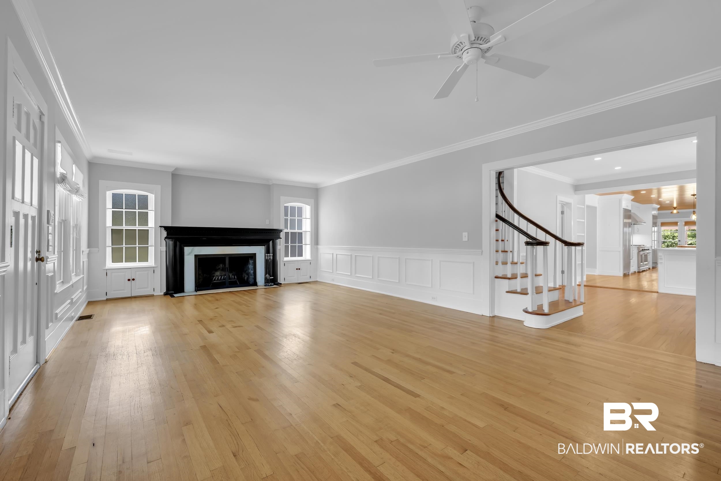 43199 Pine Grove Road Bay Minette, AL 36507 - Photo 30 of 71 Spacious room featuring hardwood flooring, a fireplace with a black mantel, white wainscoting, an elegant curved staircase, and an overhead ceiling fan