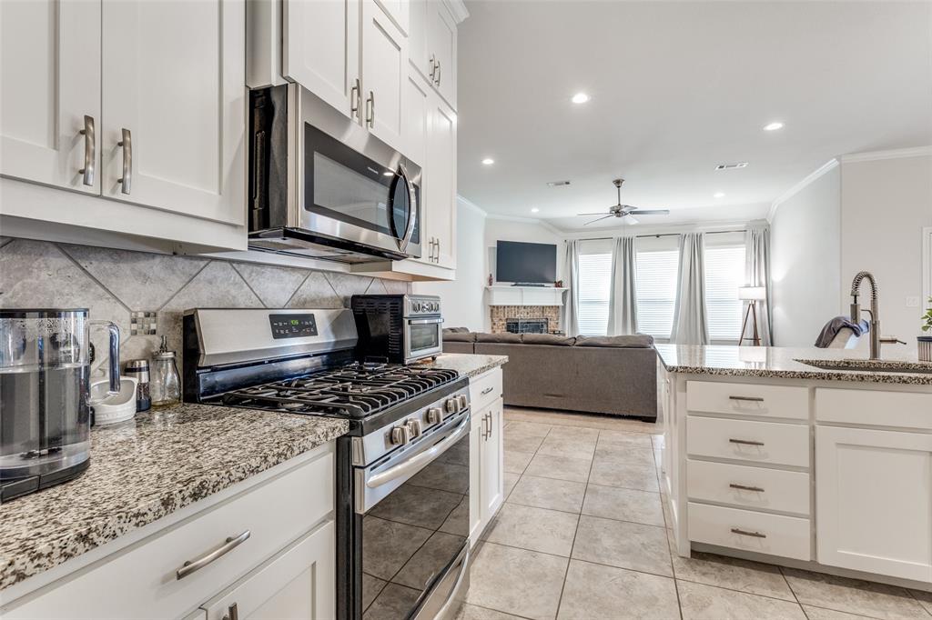 1173 Roping Reins Way Fort Worth, TX 76052 - Photo 7 of 24 Kitchen with stainless steel appliances, ornamental molding, white cabinetry, light stone counters, and a fireplace