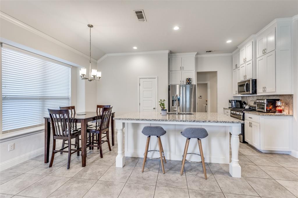 1173 Roping Reins Way Fort Worth, TX 76052 - Photo 8 of 24 Kitchen with light stone counters, stainless steel appliances, a center island with sink, white cabinetry, and ornamental molding