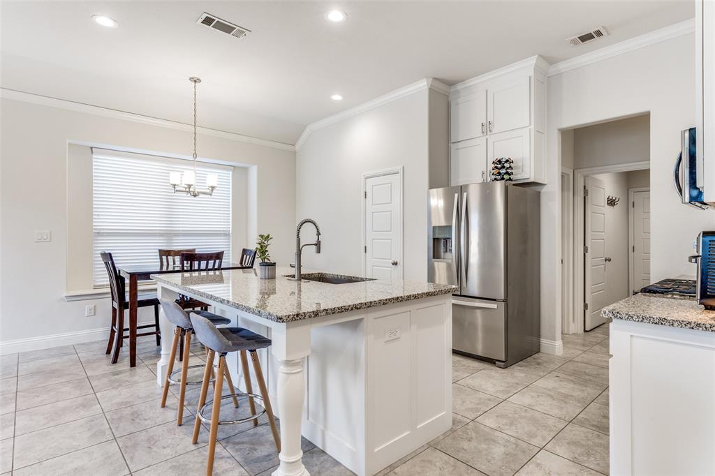 1173 Roping Reins Way Fort Worth, TX 76052 - Photo 9 of 24 Kitchen featuring light stone countertops, stainless steel appliances, a kitchen bar, white cabinetry, and ornamental molding