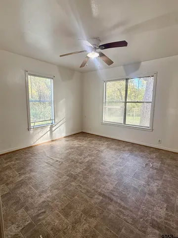 an empty room with chandelier fan and windows