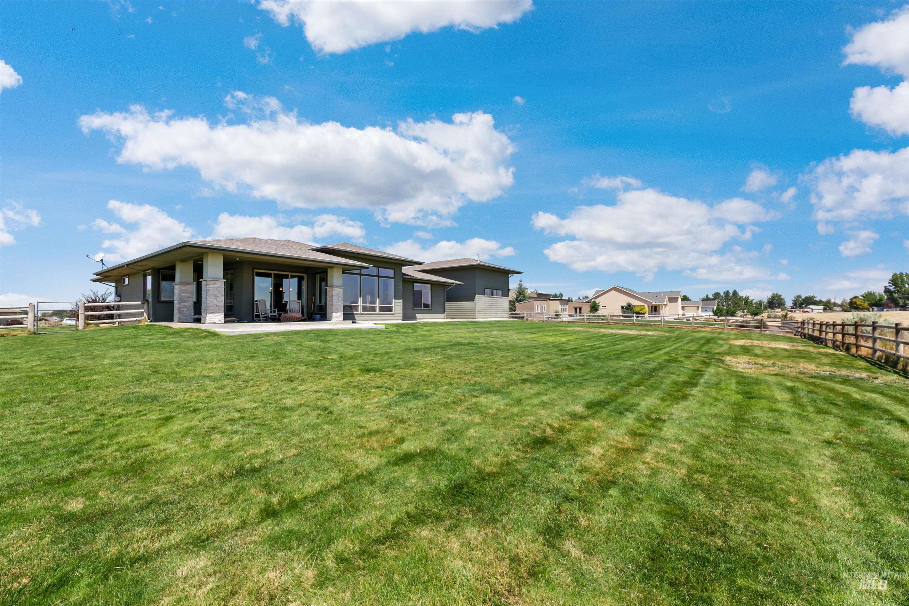 24398 Tombstone Ridge Court Middleton, ID 83644 - Photo 40 of 47 Expansive rear lawn area featuring a contemporary-style residence with multiple large windows, a sliding glass door, a paved patio, and decorative stone columns