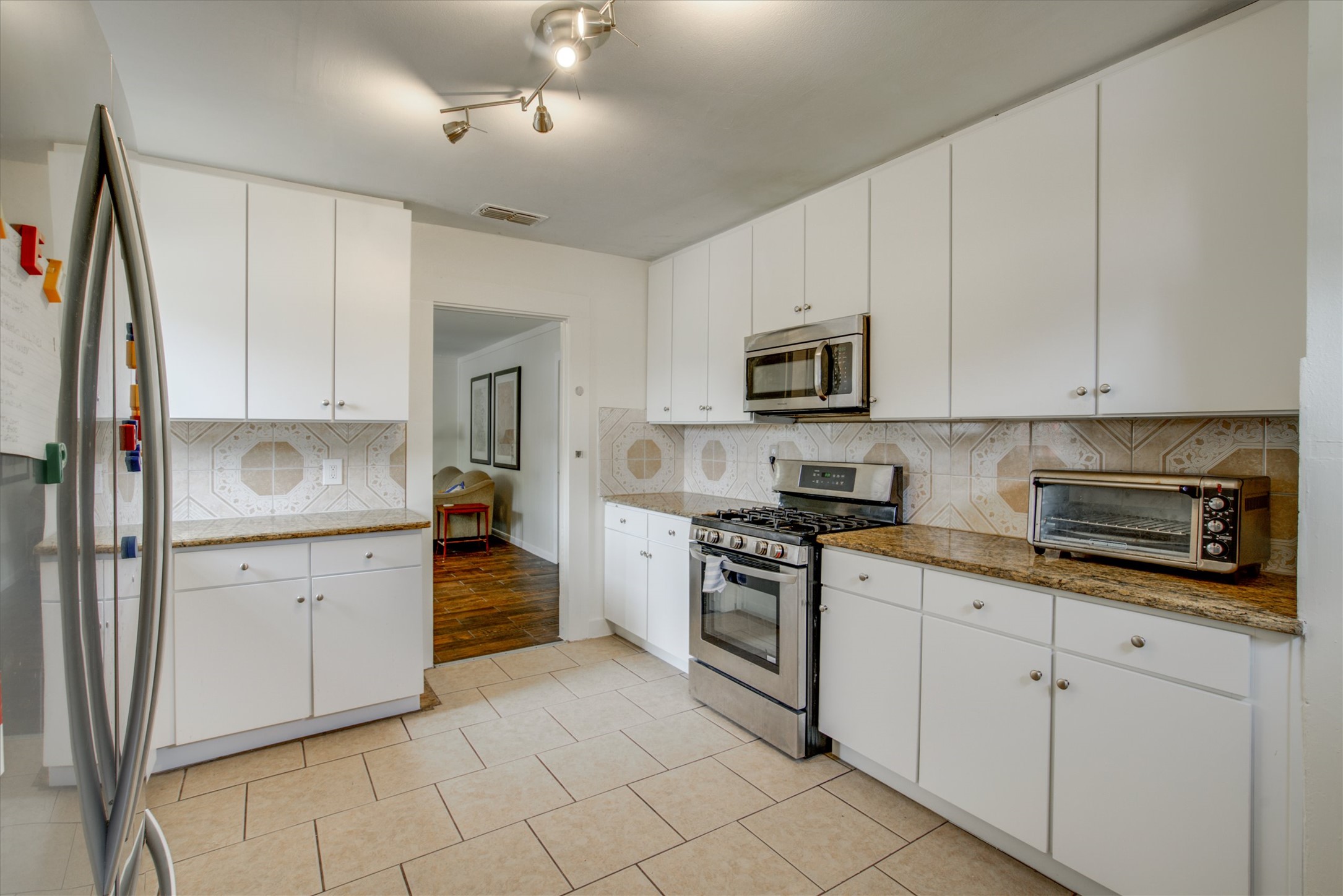 4615 Ribbecke Avenue Austin, TX 78721 - Photo 2 of 19 Kitchen featuring stainless steel appliances, white cabinetry, dark stone counters, light tile patterned floors, and tasteful backsplash
