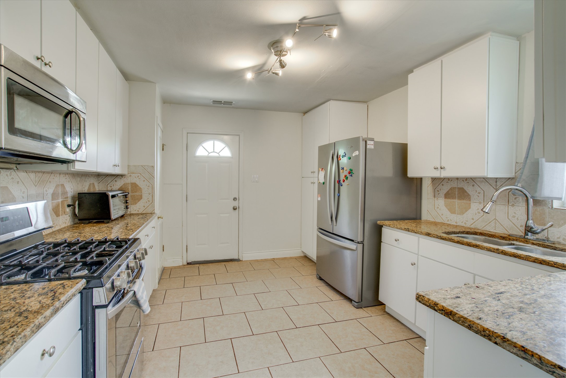 4615 Ribbecke Avenue Austin, TX 78721 - Photo 7 of 19 Kitchen featuring backsplash, stainless steel appliances, light stone counters, white cabinetry, and light tile patterned flooring
