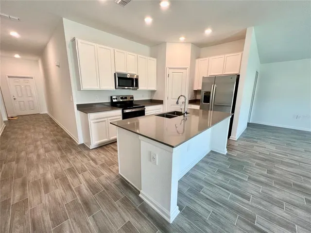 a kitchen with stainless steel appliances a stove a sink a refrigerator white cabinets and wooden floor