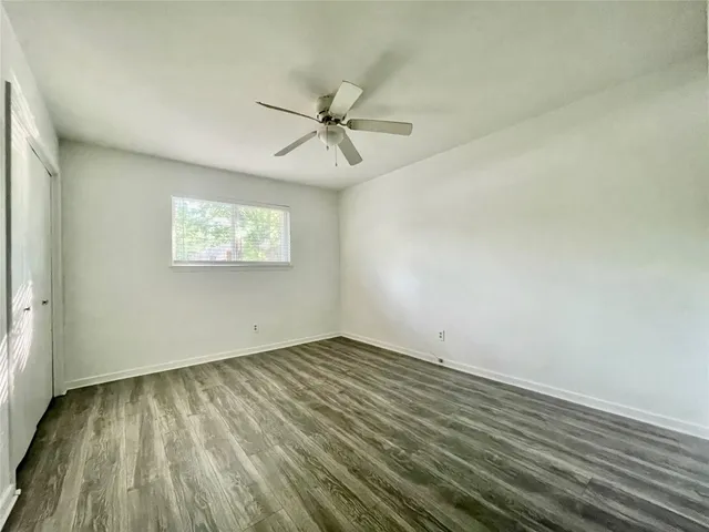an empty room with wooden floor fan and windows