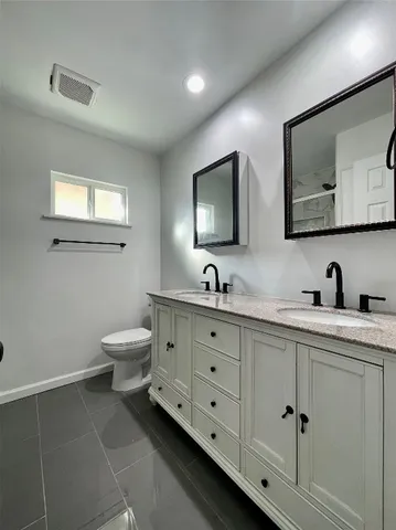 a spacious bathroom with double sink a toilet and a mirror