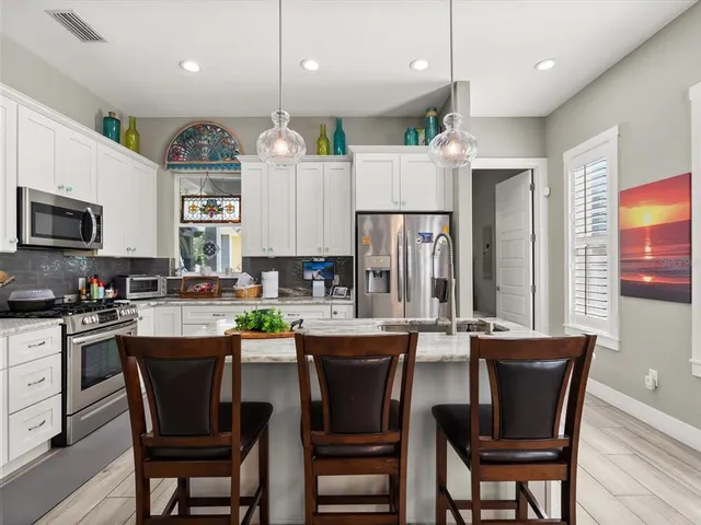 a dining area with stainless steel appliances kitchen island granite countertop a dining table chairs and a refrigerator