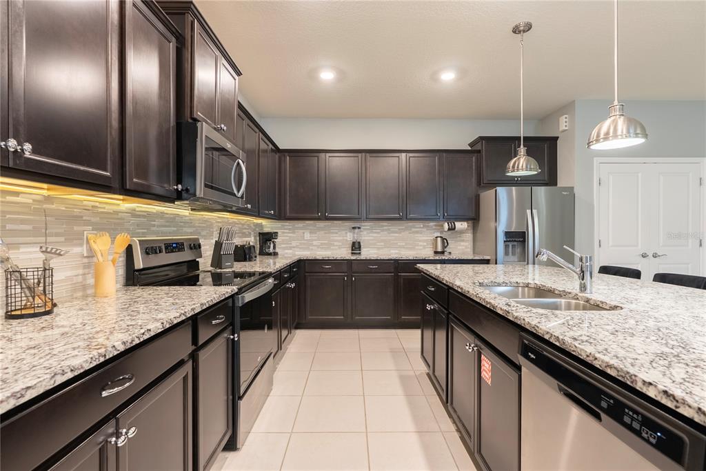 4425 Kaipo Road Davenport, FL 33897 - Photo 17 of 100 a kitchen with stainless steel appliances granite countertop a sink a stove and a wooden cabinets