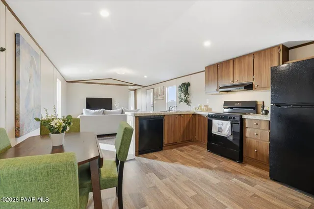 a kitchen with stainless steel appliances kitchen island granite countertop a refrigerator a stove top oven a sink dishwasher and white cabinets with wooden floor