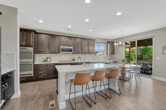 a kitchen with stainless steel appliances granite countertop a stove top oven a sink dishwasher a dining table and chairs with wooden floor